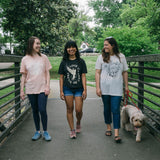 Three women with a dog walking in a park wearing Preemptive Love Spring shirts. Women's fashion and style